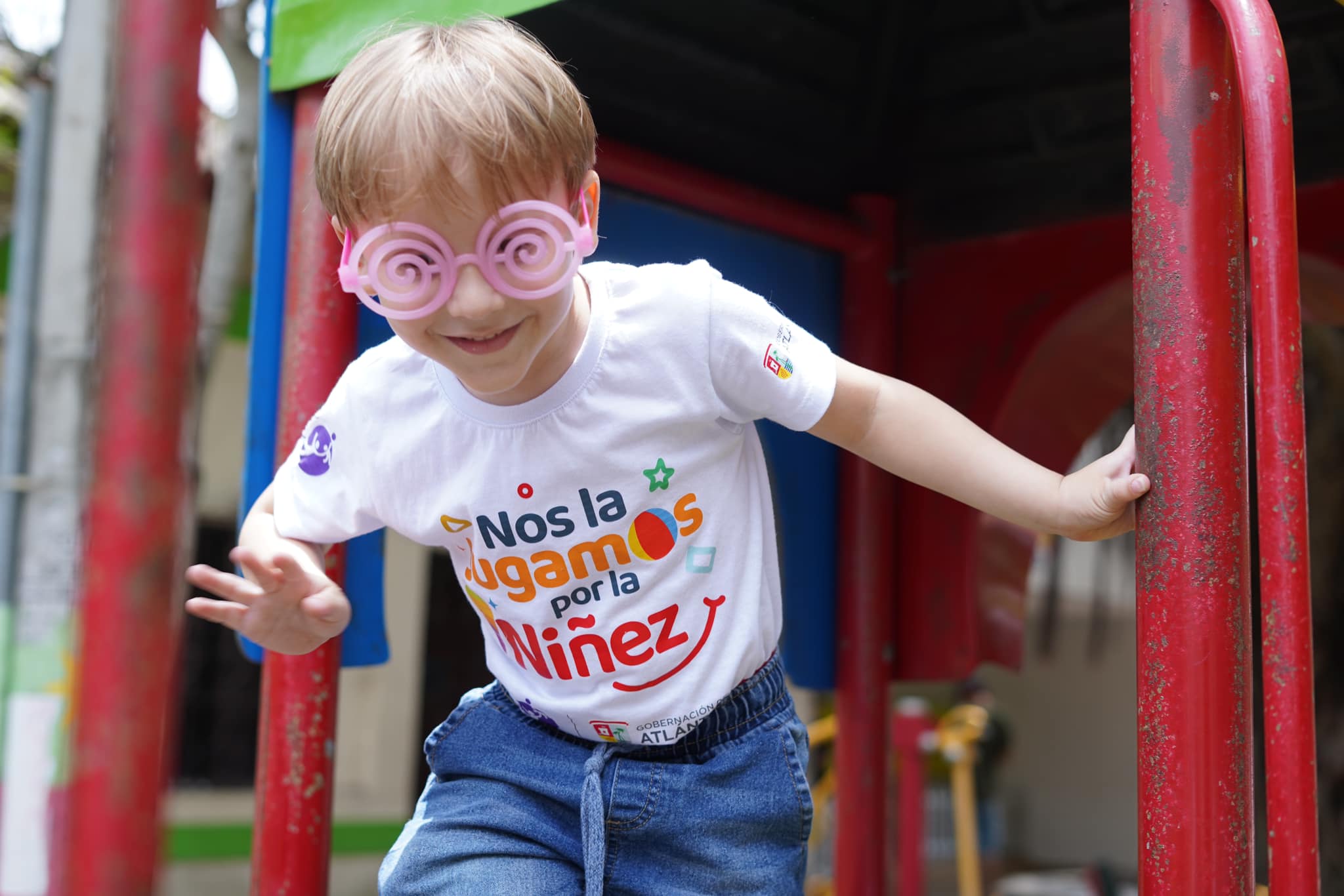 Foto de un niño sonriendo con gafas divertidas y camiseta que dice, "Nos la jugamos por la niñez"